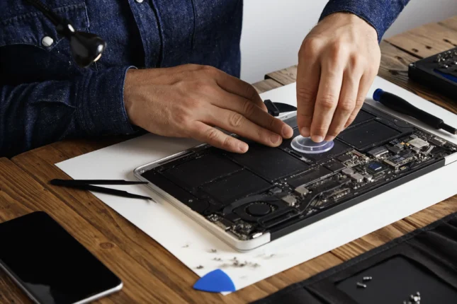 master-uses-small-suction-cup-change-battery cells from broken laptop repair clean it his laboratory with specific toolkit wooden table around